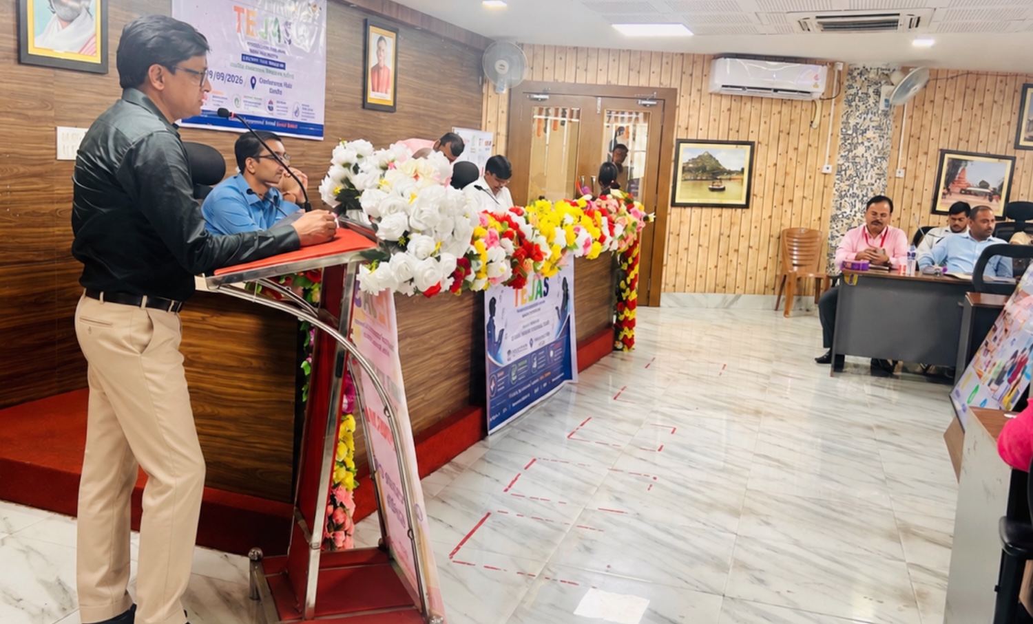 Rajeev Singh speaking into a microphone behind a flower-decorated podium with TEJAS signage.